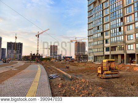 Vibro Roller Soil Compactor Leveling Ground At Construction Site. Tower Cranes And Buildings On Suns