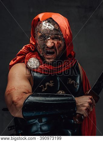 Savage Roman Slayer With Blood On His Face Dressed In Red Cloak And Weared With Mask Screams Holding
