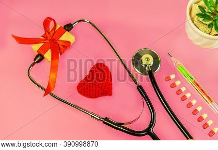 Knitted Red Heart With A Phonendoscope, A Present In A Gift Box, Pink Pills And A Thermometer On A P