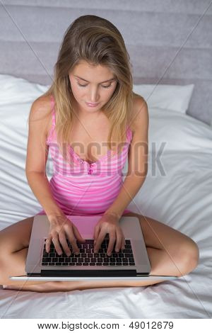 Bella bionda donna seduta sul suo letto usando il portatile a casa in camera da letto