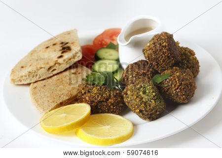 Homemade falafels (herbed and spicy chickpea balls) on a plate with Egyptian flat bread, lemon slices, tomato, cucumber and a tahina sauce.