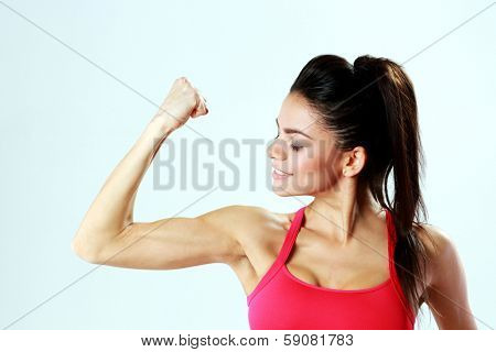 Young sport woman looking at her biceps on gray bakground