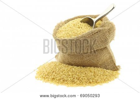 bulgur (couscous) in a burlap bag with an aluminum scoop on a white background