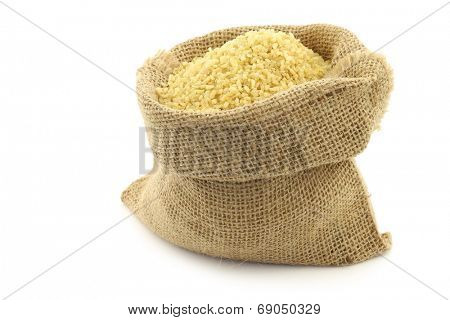 bulgur (couscous) in a burlap bag with an aluminum scoop on a white background
