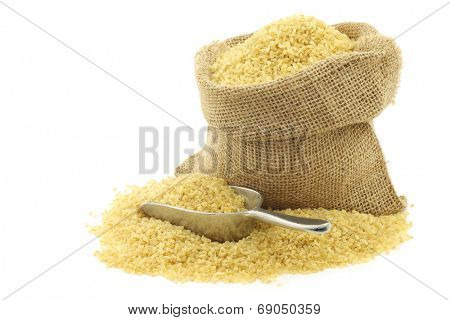 bulgur (couscous) in a burlap bag with an aluminum scoop on a white background
