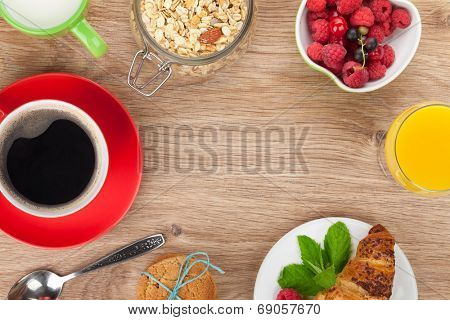 Healty breakfast with muesli, berries, orange juice, coffee and croissant. View from above on wooden table with copy space