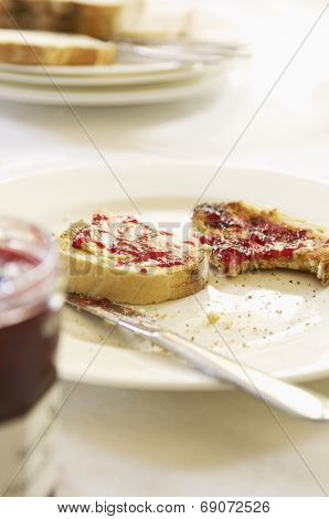 Closeup of a plate with half eaten toast covered in jam on table set for breakfast