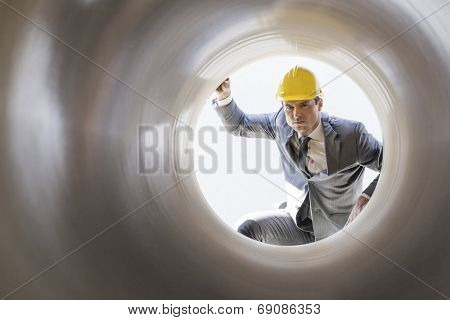 Young male supervisor examining large pipe at construction site