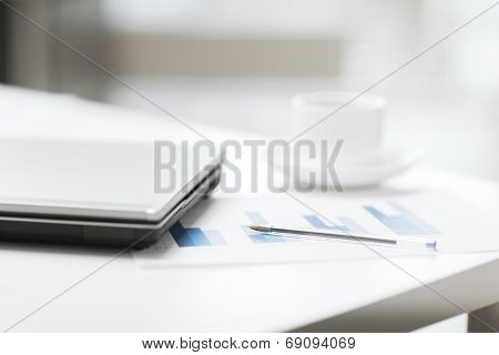 business, technology and beverage concept - close up of laptop computer, charts, pen and coffee in office