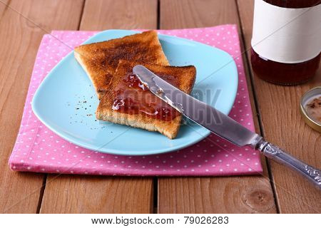 Toast bread spread with jam on plate and napkin with knife near jar on wooden table background