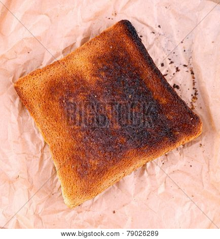 Burnt toasted bread on piece of paper and wooden table background