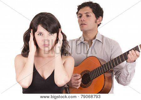 beautiful girl gesturing silence while young man serenades her with guitar