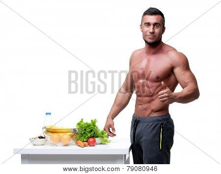 Happy muscular man standing with thumbs up near healthy food