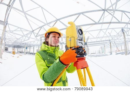 female surveyor worker working with theodolite transit equipment at road construction site outdoors
