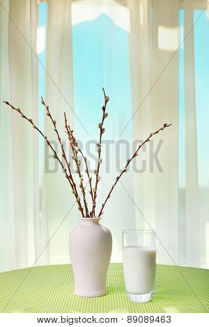 Willow twigs and glass of milk on table on curtains background