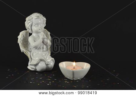 White statue of an angel and a candle, on black background