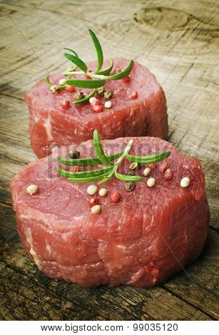 raw steak with pepper and rosemary on the wooden background