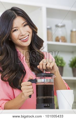 Beautiful young Asian Chinese woman or girl at home in her kitchen smiling and making a cup or mug of coffee with a french press or cafetiere