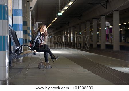 Young woman, sitting on a bench in an underground sation, waiting for her train to arrive at the platform