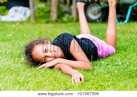 African girl playing on meadow in front of picket fence rolling around