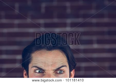 Angry man with raised eyebrows looking away against brick wall
