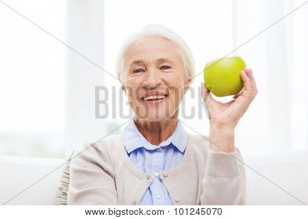 age, healthy eating, food, diet and people concept - happy smiling senior woman with green apple at home