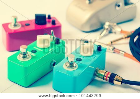 Setting up guitar audio processing effects. Electric guitar stomp box effectors and cables on studio floor. Focus is on forehand switch box