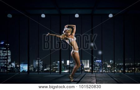 Hot young dancing woman in white bikini on night city background