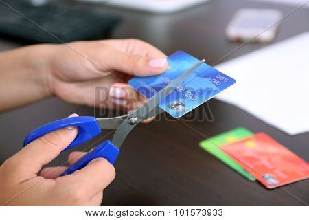 Woman's hands cutting bank card with scissors on wooden table background