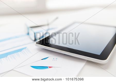 business, objects and technology concept - close up of tablet pc computer, eyeglasses and papers on office table