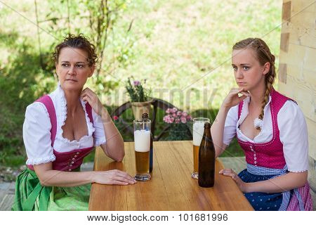 Mother And Daughter Sitting At A Table In Dirndl In Front Of A Glass Of Beer.