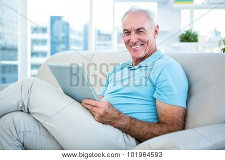 Happy senior man sitting on sofa with digital tablet at home