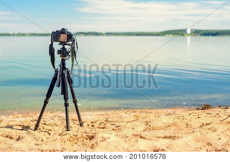 A camera on a tripod on the sandy seashore removes the seascape. Photographic equipment in the process of shooting the landscape. Camera while taking a photo or time-lapse