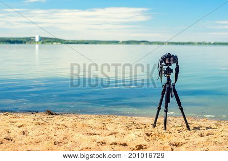 A camera on a tripod on the sandy seashore removes the seascape. Photographic equipment in the process of shooting the landscape. Camera while taking a photo or time-lapse