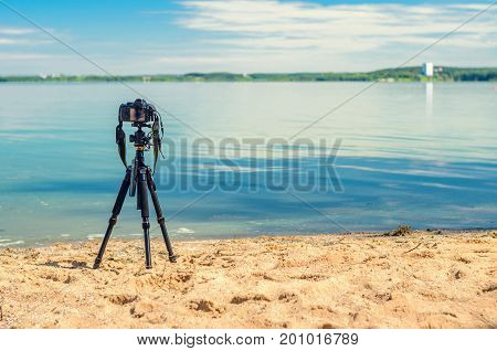 A camera on a tripod on the sandy seashore removes the seascape. Photographic equipment in the process of shooting the landscape. Camera while taking a photo or time-lapse