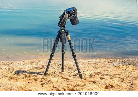Camera on a tripod near the seaside removes of seashells on the sand. Photographic equipment in the process of shooting the landscape. Camera while taking a photo or time-lapse