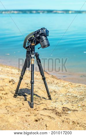 Camera on a tripod near the seaside removes of seashells on the sand. Photographic equipment in the process of shooting the landscape. Camera while taking a photo or time-lapse