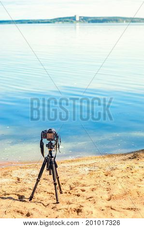 A camera on a tripod on the sandy seashore removes the seascape. Photographic equipment in the process of shooting the landscape. Camera while taking a photo or time-lapse