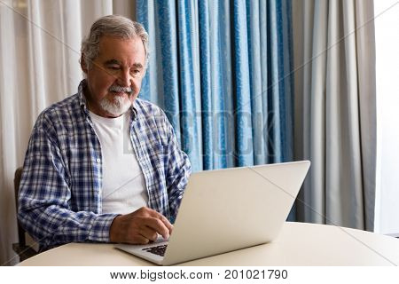 Senior man using laptop while sitting at table in nursing home