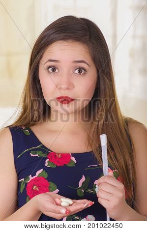 Close up of a worried young woman holding in her hand a medical object used for vaginal infection medicine and holding in her other hand a soft gelatin vaginal tablet or suppository, treatment of diseases of the reproductive organs of women in a blurred b