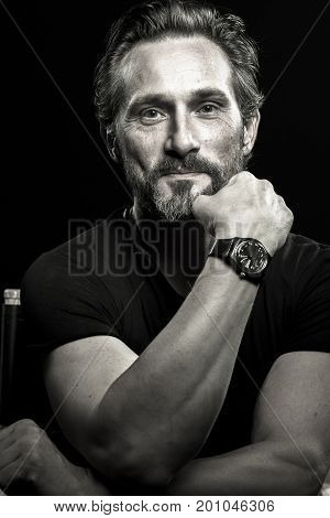 Close up portrait of satisfied man against black background. Mature man with stong look, holding hand on face.