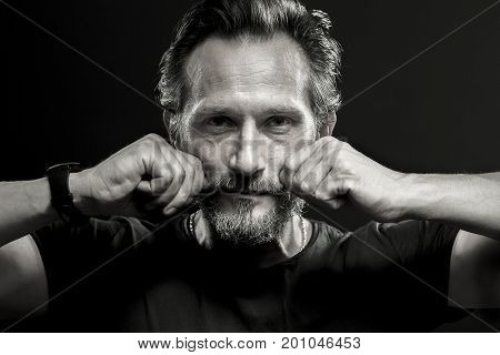 Monochrome portait of mid aged man holding fists on his cheeks. Srong man looking in camera isolated on black backgound.