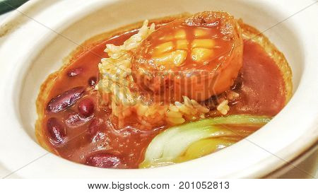 Braised Abalone in brown sauce topped with red beans, rice, vegetables in a large bowl.