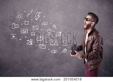 An elegant hipster guy trying to use a vintage camera with camera settings icons drawn on wall, like flash, white balace or ISO value concept