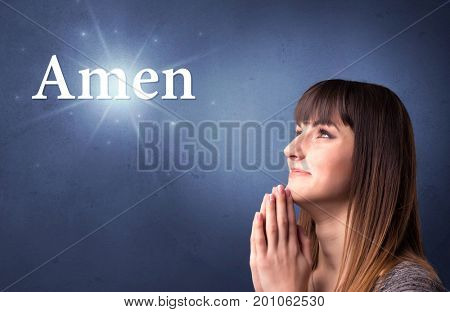 Young woman praying on a blue background with the word Amen written above her