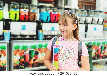 Cute little girl drinking colorful frozen slushie drink on hot summer day