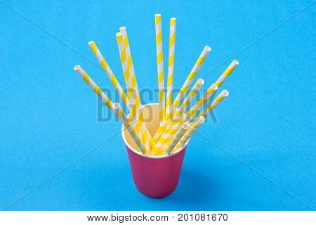 a bundle of multi-colored drinking straws in a paper Cup on a blue background. fashion minimal. flat lay