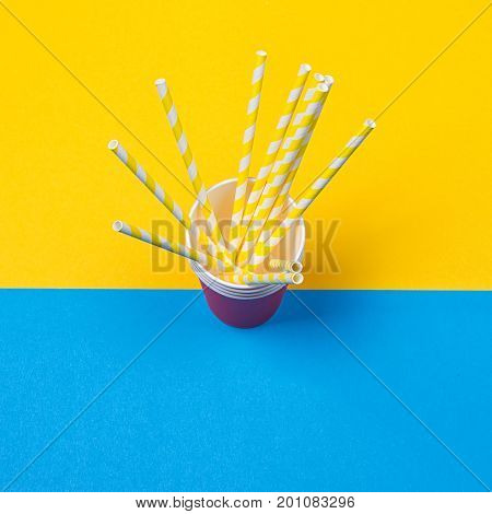 a bundle of multi-colored drinking straws in a paper Cup on a yellow and blue background. fashion minimal. flat lay