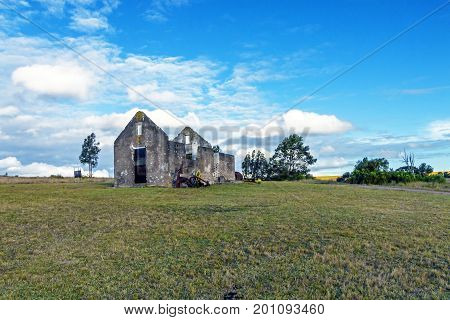 Rural old abandoned derelect farm building on dry winter landscape against blue cloudy sky 