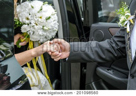 Groom holds the bride's hand out of the car.
